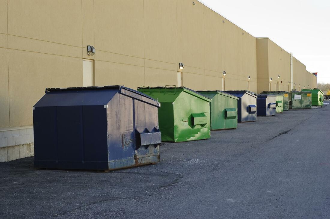 several 20 yard dumpsters in a long row bordering a building